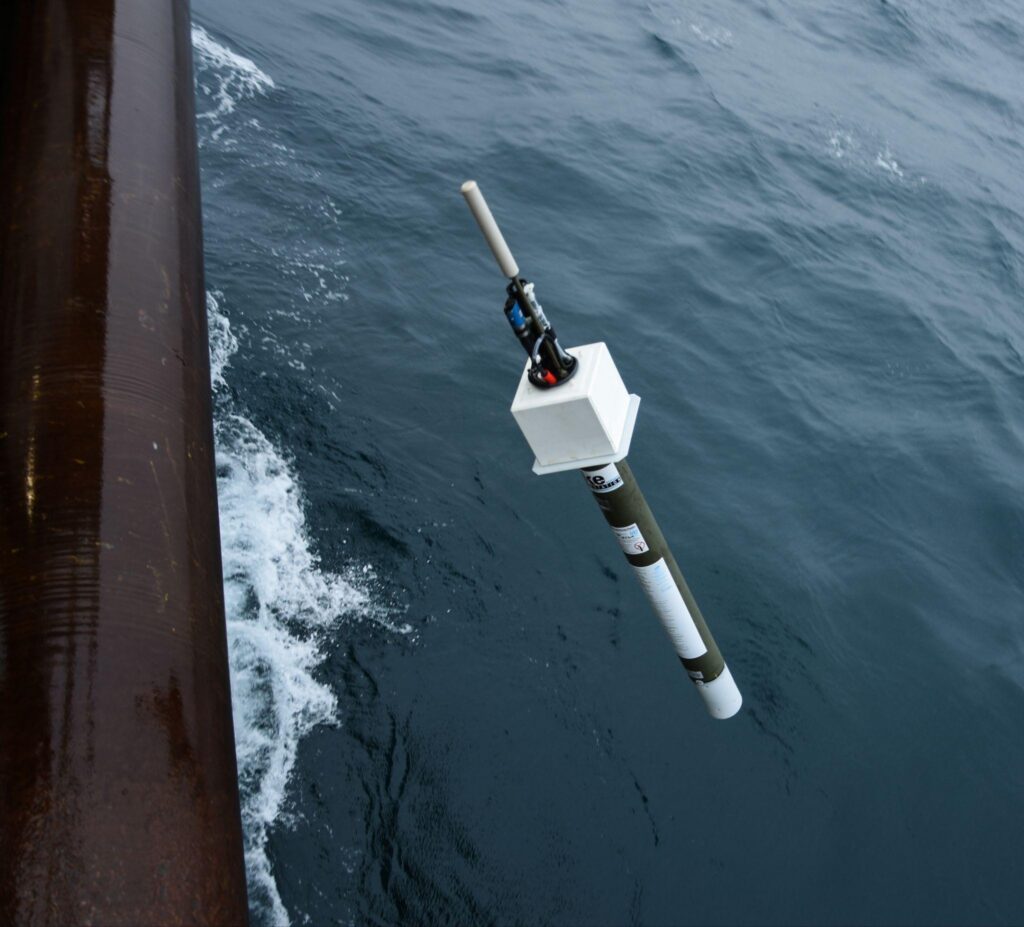 Argo float suspended above the ocean beside a research vessel during deployment.