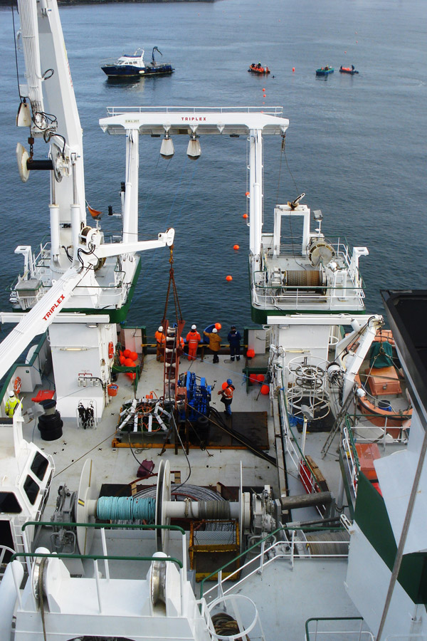 Crew working among cranes, winches and other equipment on the deck of a research vessel.
