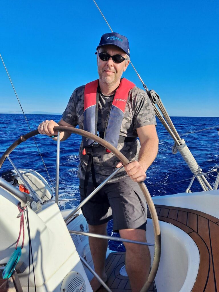 Dr Fabio Sacchetti at the helm of a sailing boat on open water.