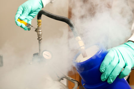 Gloved researcher handling laboratory equipment surrounded by cold vapour.
