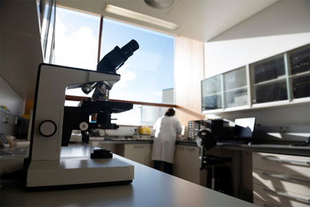 Microscope on a laboratory bench with a researcher working in the background.