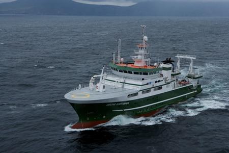 RV Celtic Explorer underway in open water with a mountainous coastline in the distance.