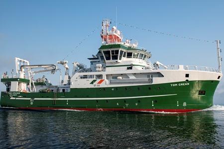 RV Tom Crean viewed broadside on calm water under a clear blue sky.