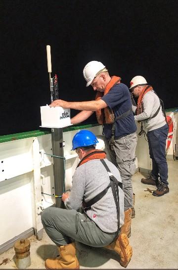 Three Marine Institute personnel in hard hats preparing an Argo float on a ship’s deck at night.